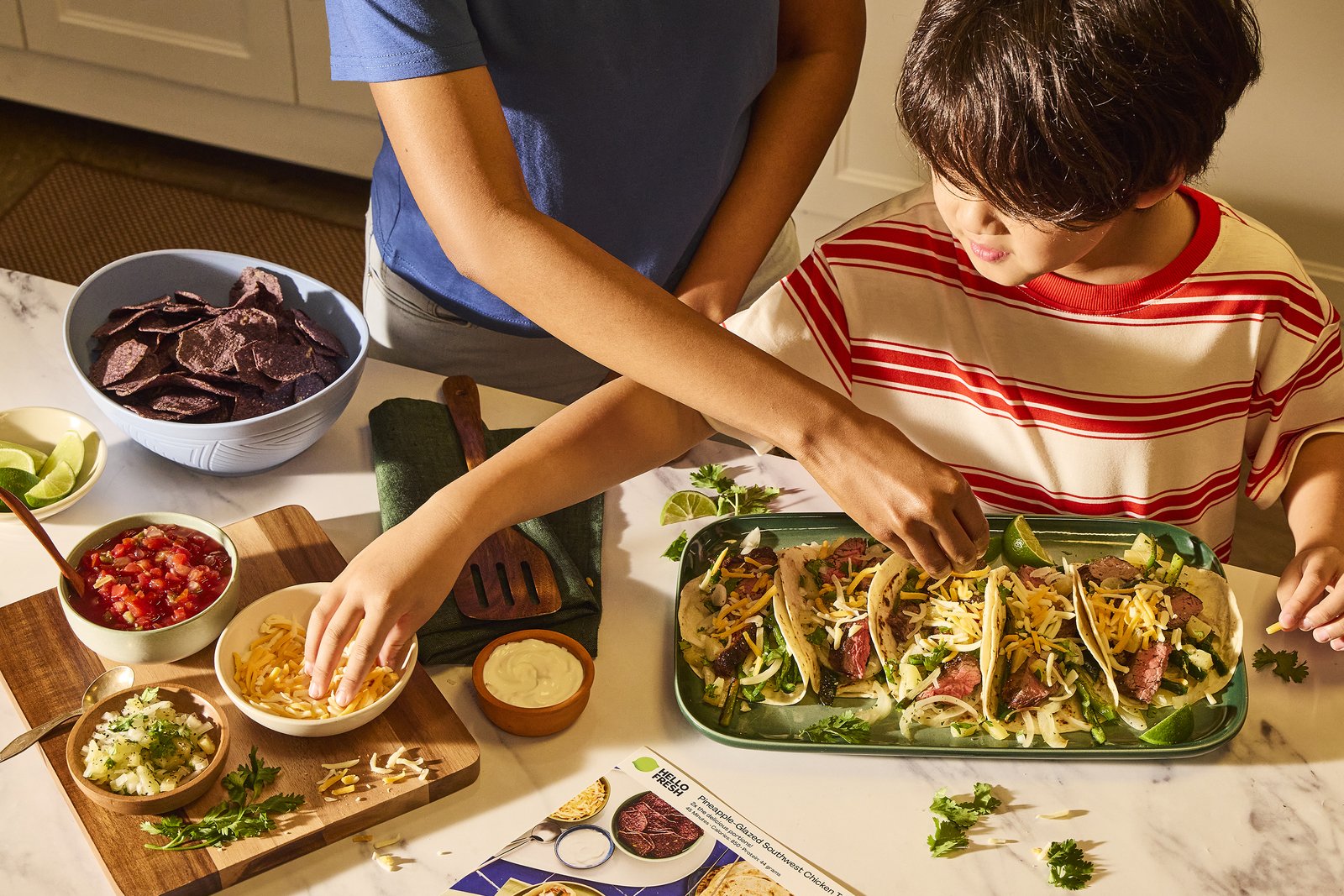 A family building tacos together at the kitchen table