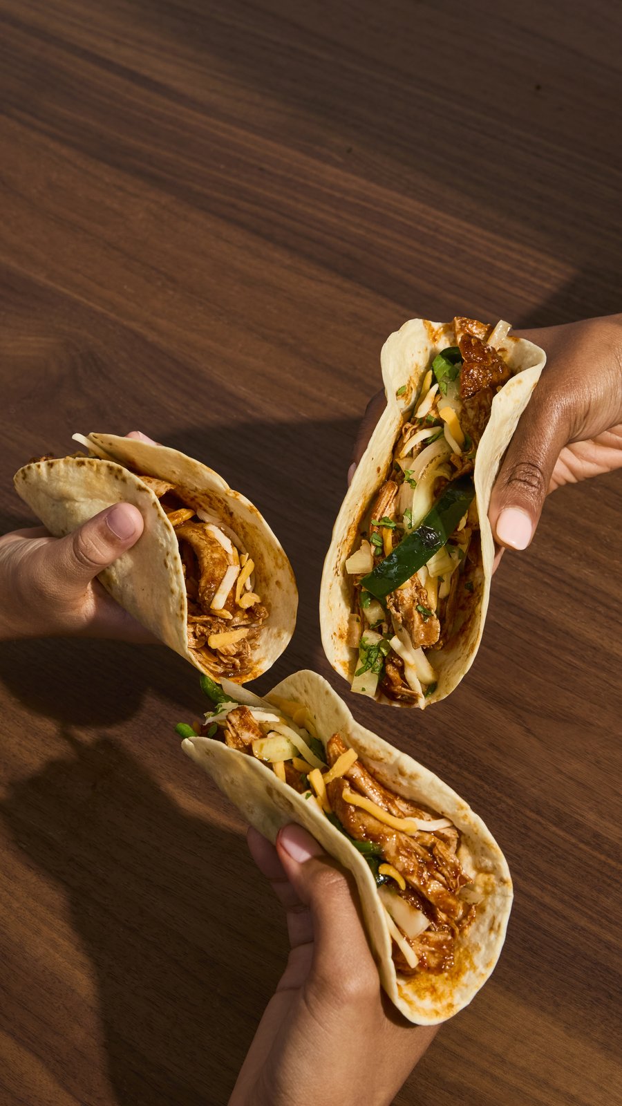 Two hands holding folded chicken tacos